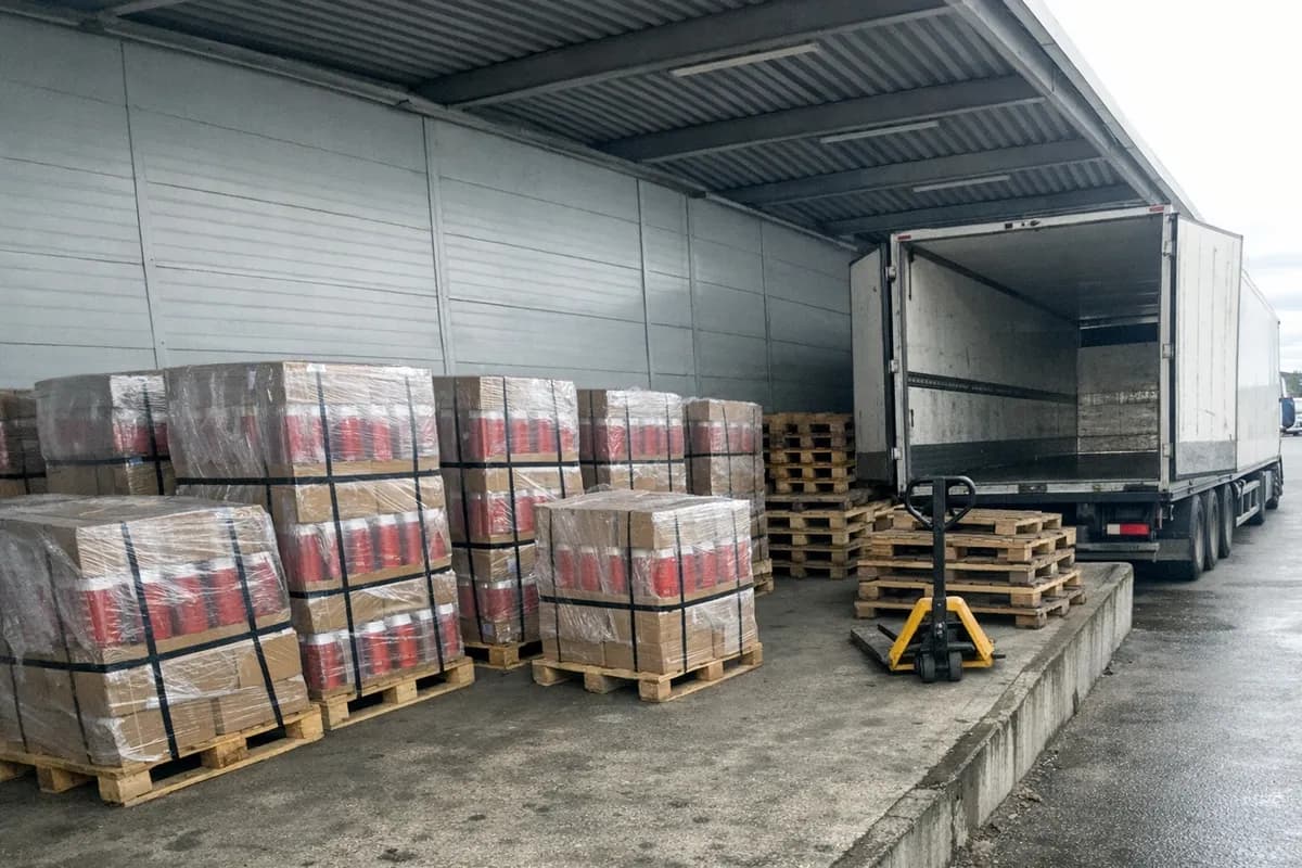 Pallets of boxed red extinguishers staged on EUR pallets at a Swedish loading dock beside a parked white trailer.